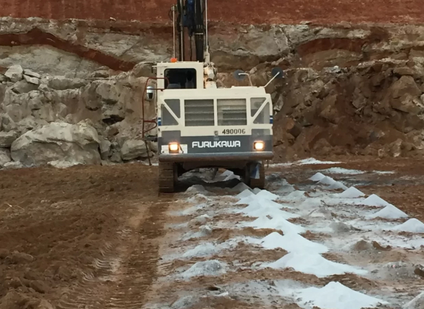 A Furukawa drilling machine operates on a construction site, surrounded by rocky terrain and a sandy surface, showcasing heavy machinery in action.